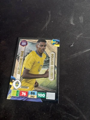 Alexander Isak Panini Adrenalyn fotbollskort Sverige - Säljer ett Panini Adrenalyn fotbollskort med svensk landslagsspelare, Limited Edition från Road to 2018 Russia. Kortet har gul och blå design, spelarens namn och statistik samt officiell logga. Perfekt för samlare av fotbollskort.