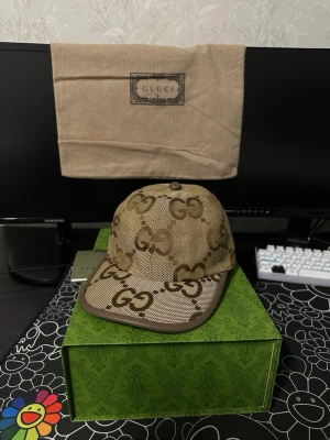 Beige GG keps  - Säljer en beige keps från Gucci med det klassiska GG-monogrammet över hela kepsen. Kepsen har böjd skärm och är tillverkad i canvasmaterial med detaljer i brunt. Insidan är fodrad i ljus textil och etiketten visar Gucci-loggan. Perfekt för dig som gillar lyxiga accessoarer.