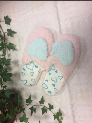 Pastellfärgade fluffiga tofflor - Supersöta tofflor i pastellrosa med ljusblå fluffiga hjärtan på ovansidan. Insidan har ett vitt tyg med blåa hjärtmönster. Tofflorna är gjorda i mjukt, lurvigt material som känns riktigt mysigt på fötterna. Perfekta för att chilla hemma och hålla värmen.
