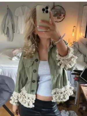 Grön Zara jacka med virkade detaljer, fransar - Snygg ljusgrön jacka med virkade och fransiga detaljer i vitt längs ärmslut och nederkant. Jackan har knappar framtill, två bröstfickor och en croppad passform. Perfekt för dig som vill sticka ut med en unik och trendig look.