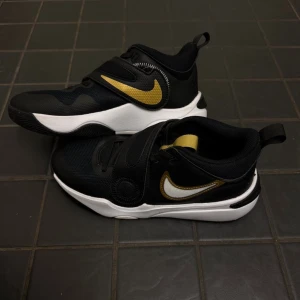 Säljer ett par Nike Team Hustle D 11 (GS) Black/Metallic Gold – Size 40 EU - Skorna är använda endast 2 gånger och är i mycket fint skick. Inga synliga skador eller större slitage.  Bekväma och smidiga skor med kardborreband för enkel av- och påtagning. Originalkartong medföljer ej.  Size: 40 EU 🏷️ Rabatt vid köp av flera par skor!