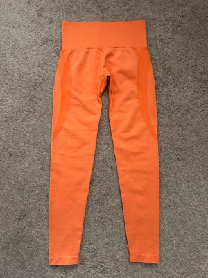 Orange seamless leggings från NVGTN - Säljer ett par orange seamless leggings från NVGTN med hög midja och tight passform. Materialet är stretchigt och mjukt, perfekt för träning eller chill. Diskreta detaljer längs sidorna och logga bak i midjan. Supersnygga och bekväma💗 Använda endast 1 gång!