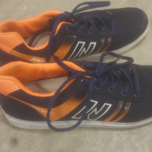 Marinblå och orange sneakers Panda - Snygga sneakers från Panda i marinblått tyg med orange detaljer och vita ränder på sidan. Skorna har vita sulor och klassisk snörning. Insidan är fodrad i orange tyg och yttermaterialet är textil. Perfekta för en sportig och avslappnad stil.