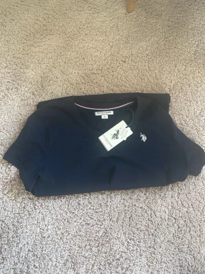 Mörkblå t-shirt från U.S. Polo Assn. - Snygg mörkblå t-shirt från U.S. Polo Assn. med klassisk passform och liten broderad logga på bröstet. Tillverkad i mjuk bomull och har rund halsringning. Perfekt för en clean och stilren look. Aldrig använd med prislapp kvar. 