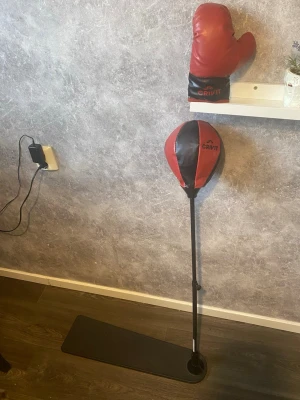 Boxningsboll med handske Crivit barn - Boxningsboll på stång från Crivit i svart och rött konstläder, perfekt för träning hemma. Medföljer en röd och svart boxningshandske i samma märke. Ställningen har en rektangulär fot för stabilitet.