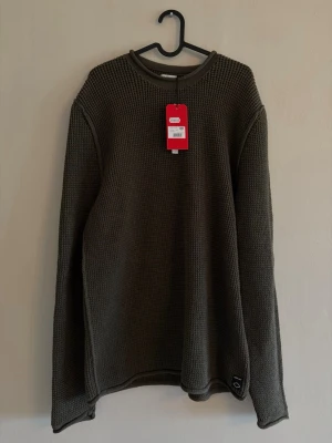 Olivgrön stickad tröja XL - Säljer en olivgrön stickad tröja i grovstickat material. Tröjan har rund halsringning och långa ärmar. Enkel och stilren design utan mönster, perfekt för dig som gillar en avslappnad look.