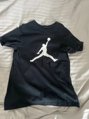 Svart Jordan t-shirt med logga - Snygg svart t-shirt från Jordan med den klassiska vita Jumpman-loggan tryckt på bröstet. T-shirten har rund halsringning och korta ärmar. Perfekt för dig som gillar sportig och stilren streetwear.