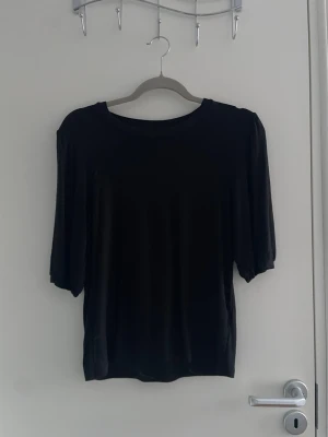 Svart topp med halvlånga puffärmar - En enkel svart topp med rund halsringning och halvlånga puffärmar. Tunn och mjuk i materialet, perfekt att styla till olika looks. Passar dig som gillar en clean och stilren vibe.