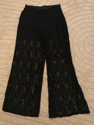 Svarta spetsleggings från La Vie - Snygga svarta leggings från La Vie by Charlotte Perrelli med bred resår i midjan och transparent spets från låret och ner. Vida ben ger en trendig look och materialet är stretchigt och bekvämt. Perfekta för dig som vill sticka ut lite extra.