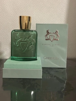 Parfums de Marly Greenley EdP 125ml - Lyxig parfym från Parfums de Marly, Greenley EdP, i en elegant grön glasflaska med guldfärgat lock. Flaskan har en rektangulär form och dekoreras med två hästar och en sköld i relief. Kommer i matchande grön ask med silverdetaljer.