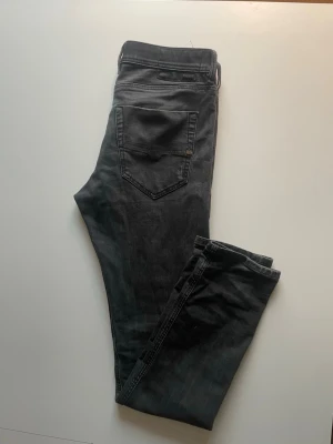 Grå svarta slim fit jeans från Diesel - Snygga grå svart slim fit jeans från Diesel med klassisk femficksdesign och diskreta slitningar. Jeansen har normal midja och smala ben, perfekta för en trendig och avslappnad look. Materialet är mjukt och stretchigt för extra komfort.