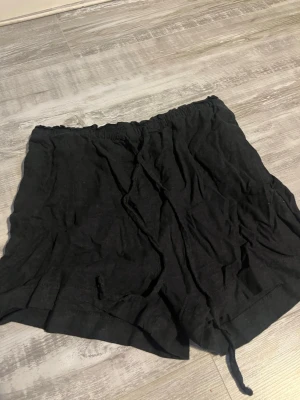 Svarta shorts från H&M med snörning - Svarta shorts från H&M med elastisk midja och snörning framtill. Tillverkade i ett mjukt och lätt material som passar perfekt för varma dagar. Enkel och avslappnad design som är lätt att matcha med olika toppar.