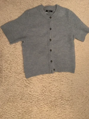 Ljusblå kortärmad kofta Gina Tricot - Kortärmad kofta i ljusblått från Gina Tricot. Koftan har rund halsringning, ribbade kanter och knappar framtill. Materialet är mjukt och stickat, perfekt för lager på lager och en chill look.