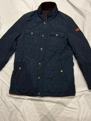 Hampton Republic jacka blå - Snygg mörkblå quiltad Hampton Republic jacka med bruna detaljer på armbågar och krage. 