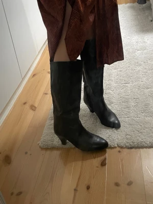 Svarta knähöga läderstövlar - Snygga svarta stövlar i läder med spetsad tå och lagom klack. Stövlarna är knähöga och har en klassisk, tidlös design som passar till många olika outfits. Sulan är omklackad och använda 1 gång sen dess. Perfekta för dig som vill ha en stilren look med edge! Strl 37