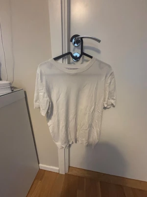 Vit kortärmad topp i bomull - En enkel och stilren vit topp med rund hals och korta ärmar. Tillverkad i mjuk bomull med ribbade muddar vid ärmsluten för en clean look. Perfekt att matcha med jeans eller kjol för en avslappnad vibe.