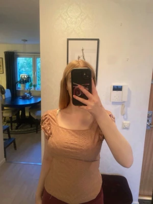 Beige topp med puffärmar och spetsdetaljer - Söt beige topp med puffiga kortärmar och fyrkantig ringning. Toppen har fina spetsdetaljer och är figurnära i modellen. Perfekt för dig som gillar romantisk och feminin stil. Beige/rosa färg