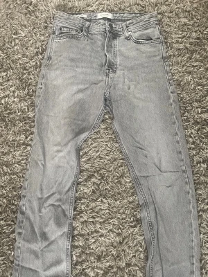 Grå loose fit jeans LOOSE/CHRIS - Säljer ett par grå loose fit jeans med rak passform och klassisk femficksdesign. Jeansen har en avslappnad look och är tillverkade i denim. Perfekta för dig som gillar en bekväm och trendig stil.