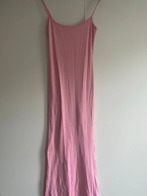 Lång rosa slipklänning med smala band - En enkel och stilren lång slipklänning i ljusrosa med smala axelband. Klänningen har en rak och slimmad passform som följer kroppen och är tillverkad i ett mjukt och stretchigt material. 