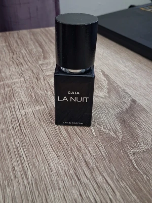 CAIA La Nuit Eau de Parfum 15 ml - Snygg miniatyr parfymflaska från CAIA i modellen La Nuit. Flaskan är svart och fyrkantig med ett stilrent, minimalistiskt utseende och har en svart cylinderformad kork. Texten på flaskan är vit och den har en metallisk sprayfunktion. Perfekt för dig som gillar exklusiva dofter. Doft - kvällsdoft med mandarin, persika, svart viol, ros,  vanilj, patcholi och kanel.