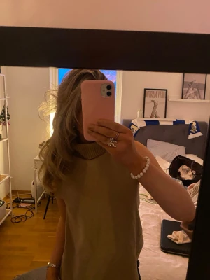 Beige stickad polotopp - Säljer en beige stickad polotopp med ärmlös design och hög krage. Perfekt för att skapa en chill och snygg look, passar till både jeans och kjol. Materialet är mjukt och ger en skön känsla. Toppen har en loose passning och är enkel att matcha.