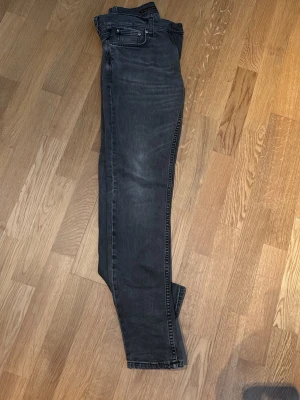 Svarta Nudie Lean Dean jeans  - Säljer ett par svarta slim fit jeans med klassisk femficksmodell och dragkedjegylf. Jeansen har en snygg tvättad look med lätt slitningar på låren och knäna. Perfekta för dig som gillar en stilren och modern vibe.