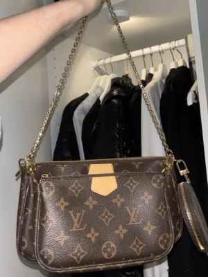 Väska - Snygg handväska i brunt monogrammönster med guldiga detaljer och kedjerem. Väskan har flera fack med dragkedja och en liten rund coin pouch. Superfin och väldigt bra skick, dragkedjorna funkar helt perfekt.