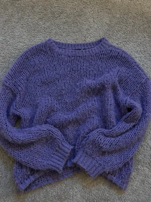 Lila chunky stickad tröja - Mysig lila stickad tröja med oversized passform och grovstickad struktur. Tröjan har rund halsringning, långa ärmar och ribbade muddar vid ärmslut och nederkant. Perfekt för kalla dagar när du vill vara både bekväm och snygg.