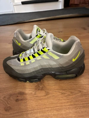 Nike Air Max 95 Neon - Nike Air Max 95 Neon med ikoniska neondetaljer, grå och svarta paneler samt mesh och mocka på ovandelen. Synlig Air-enhet i sulan och klassisk snörning. Perfekt för dig som gillar retrovibbar och streetwear.