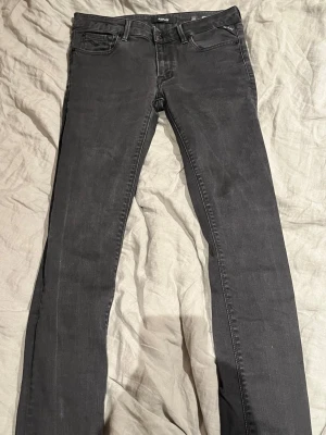 Svarta jeans från Replay - Säljer ett par svarta jeans från Replay med klassisk femficksmodell och raka ben. Jeansen har bälteshällor, knappgylf och Replay-logga på fickan. Materialet är mjukt denim som sitter snyggt och passar till många olika stilar.