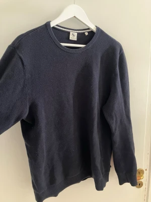Mörkblå stickad tröja från Jack’s - Klassisk mörkblå stickad tröja från Jack’s med rund halsringning och ribbade muddar vid ärmslut och nederkant. Tröjan har en enkel och stilren design, perfekt för lager på lager och passar till det mesta. Materialet känns mjukt och bekvämt.