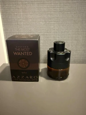 Azzaro The Most Wanted Parfum - Azzaro The Most Wanted Parfum i en cool, mörk flaska med svart och bronsfärgad design. Flaskan har en unik, cylinderformad look med metalliska detaljer och kommer i originalkartong. Perfekt för dig som gillar exklusiva och maskulina dofter.