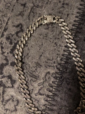 Silverfärgat cuban chain halsband - Köpte den för 1500kr säljer den för 500!!!!! Helt sjukt men jag har för många smycken.Köpte den från London butik Watches of Mayfair- London. Säljer ett chunky halsband i cuban chain-stil, silverfärgat och täckt med gnistrande stenar för en riktigt blingad look. Länkarna är breda och halsbandet har ett rejält lås med stenar även där. Perfekt för dig som vill sticka ut och addera extra shine till din outfit.