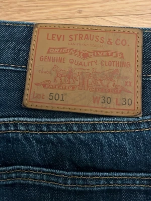 Levi's 501 blå jeans W30 L30 - Klassiska blå Levi's 501 jeans i rak modell med fem fickor och gul kontrastsöm. Tillverkade i slitstark denim med den ikoniska läderlappen bak i midjan och röd Levi's-tagg på bakfickan. Perfekta för en avslappnad och tidlös stil. Priset kan diskuteras!