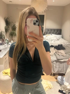 Mörkgrön v-ringad topp från Bik Bok - Snygg mörkgrön topp från Bik Bok med djup v-ringning och korta ärmar. Modellen är figurnära och har rynkade detaljer vid midjan 