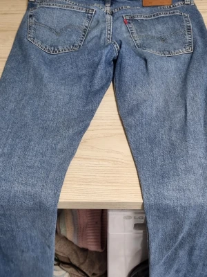 Levi's blå raka jeans - Klassiska blå jeans från Levi's 510 W33 L34 med raka ben och femficksmodell. Jeansen har en ljus tvätt och synliga slitningar för en avslappnad look. Tillverkade i bomull med Levi's ikoniska läderpatch bak i midjan.