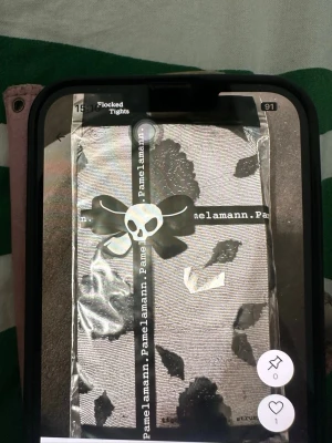 Mönstrade tights från Pamela Mann - Snygga tights från Pamela Mann med svart flockat blommönster på grå botten. Tightsen har en cool döskalle-detalj på förpackningen och är perfekta för att ge outfiten en unik touch.