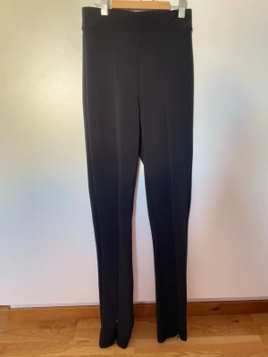 Svarta raka kostymbyxor - Säljer ett par svarta kostymbyxor med hög midja och raka ben. Snygg detalj i mitten. Perfekta till en snygg outfit när du vill känna dig extra uppklädd.