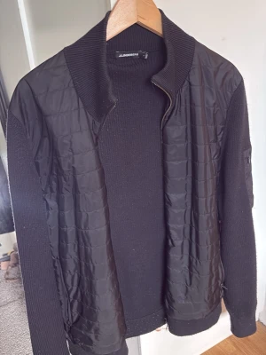 Svart Cardigan jacka från J.Lindeberg - Snygg svart Cardigan jacka från J Linderberg, använd från och till men fortfarande i väldigt bra skick! Tröjan har hög krage och dragkedja framtill. Hör av er vid intresse!