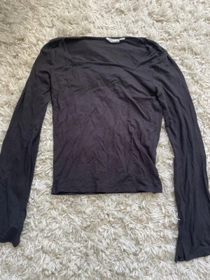 Svart långärmad topp - En enkel och stilren svart långärmad topp från Weekday. Modellen är tight med en rak halsringning och tillverkad i mjuk bomull. Perfekt att matcha med jeans eller kjol för en clean look.