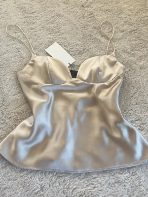 Champagnefärgad satinlinnetopp - Populär slutsåld topp från Zara. Helt ny enbart testad med lappen kvar. Den passade mig perfekt i storlek M även fast jag alltid har S i toppar men kände inte att det var min stil därför säljer jag vidare den🥰