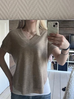 Beige stickad tröja från WERA - Säljer en beige stickad tröja med korta ärmar och v-ringning. Tröjan har en avslappnad passform och ribbade kanter vid hals, ärmslut och nederkant. Använd 1 gång, 100% ull💓Storlek S men sitter som XS
