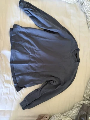 Blå sweatshirt med rund hals - En enkel blå sweatshirt med rund hals och långa ärmar. Tröjan har ribbade muddar vid ärmslut och nederkant. Perfekt för en avslappnad stil och passar till det mesta. Materialet känns mjukt och bekvämt mot huden.