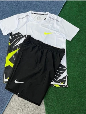 Nike sportset t-shirt och shorts - Säljer ett sportigt set från Nike med en vit t-shirt med neongult swoosh och grafiskt mönster i svart, vitt och gult. Tillhörande svarta shorts med vit Nike-logga och elastisk midja. Perfekt för träning eller gympass.