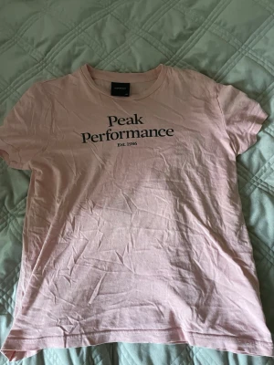 Rosa Peak Performance t-shirt - Säljer en ljusrosa t-shirt från Peak Performance med svart tryck framtill. Klassisk rund halsringning och korta ärmar. Tillverkad i mjuk bomull som är skön att bära. Perfekt för en avslappnad och stilren look. Älskade verkligen denna men den har växt ur mig så måste tyvärr sälja.