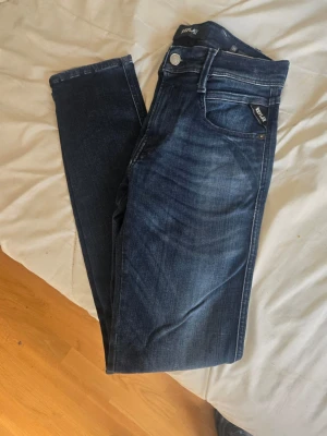 Mörkblå Replay jeans slim fit - Snygga mörkblå jeans från Replay med slim fit passform. Klassisk femficksmodell med Replay-logga på fickan och detaljerade sömmar. Jeansen har en lätt tvättad look och är tillverkade i mjukt denimtyg för skön känsla. W28 L32