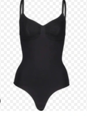 Svart body med smala axelband - Stilren svart body med smala axelband och markerade kupor. Figurnära passform som framhäver siluetten. Perfekt att bära under kläder eller som ett statement-plagg. Materialet ser ut att vara stretchigt och bekvämt, troligen i en blandning av syntetfiber.