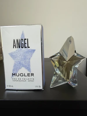 Angel Eau de Toilette från Mugler - Angel Eau de Toilette från Mugler, 30 ml. Sprayade 2-3 gånger för testning. Flaskan är formad som en stjärna i transparent glas med silverdetaljer. Förpackningen är vit med en blå stjärna och svart text. Perfekt för dig som gillar unika och snygga parfymflaskor.
