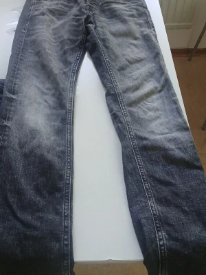 Svarta tvättade jeans Jack & Jones - Säljer ett par svarta jeans från Jack & Jones med snygg tvättad effekt och raka ben. Klassisk femficksmodell och knappgylf. Perfekta till en avslappnad streetstil. Materialet är bomull med lite stretch för extra komfort.
