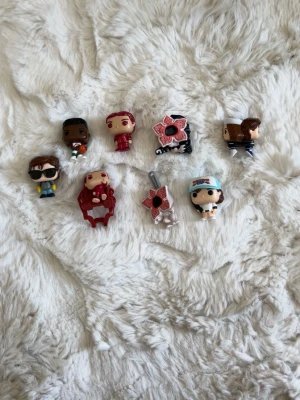 Stranger Things Funko Pop-nyckelringar - Samling med åtta små Funko Pop-figurer ifrån kinder ägg och nyckelringar inspirerade av Stranger Things. Flera karaktärer och monster i olika färger, bland annat röd, blå, brun och svart. Figurerna är tillverkade i plast och har typiska stora huvuden och små kroppar. 
